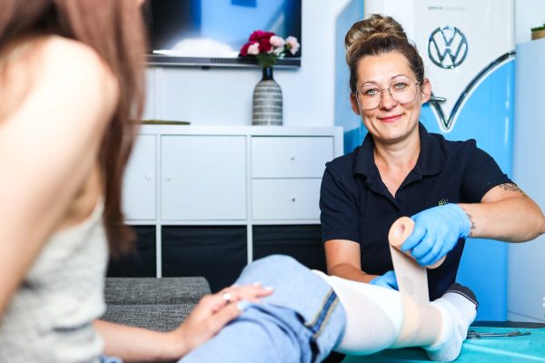 1gradmehr Pflegerin pflegt eine Verletzung am Fuß einer Dame bei Ihr in der Küche