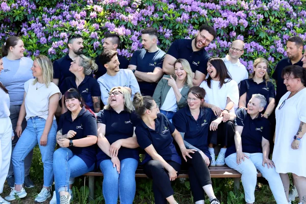 Gesamtes Teambild von 1gradmehr Mitarbeitern vor einer Blumenlandschaft in Lila